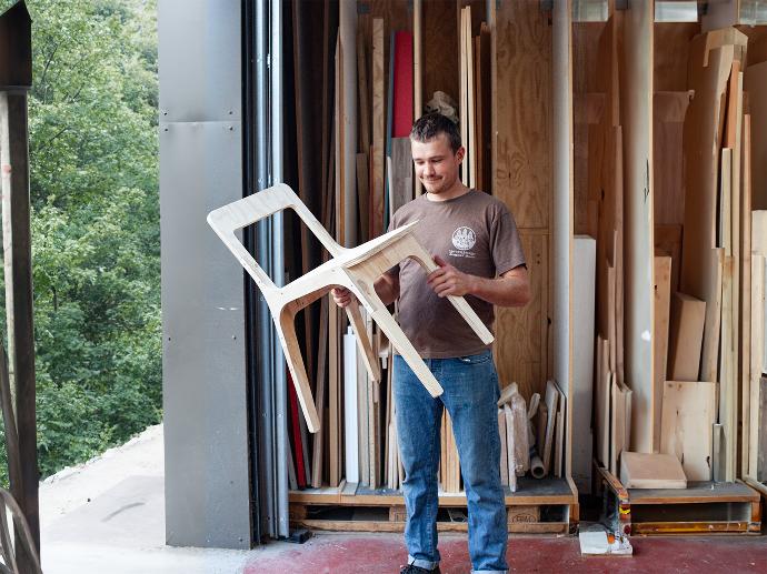 Julien standing in Microfactory workshop and holding his new chair prototype