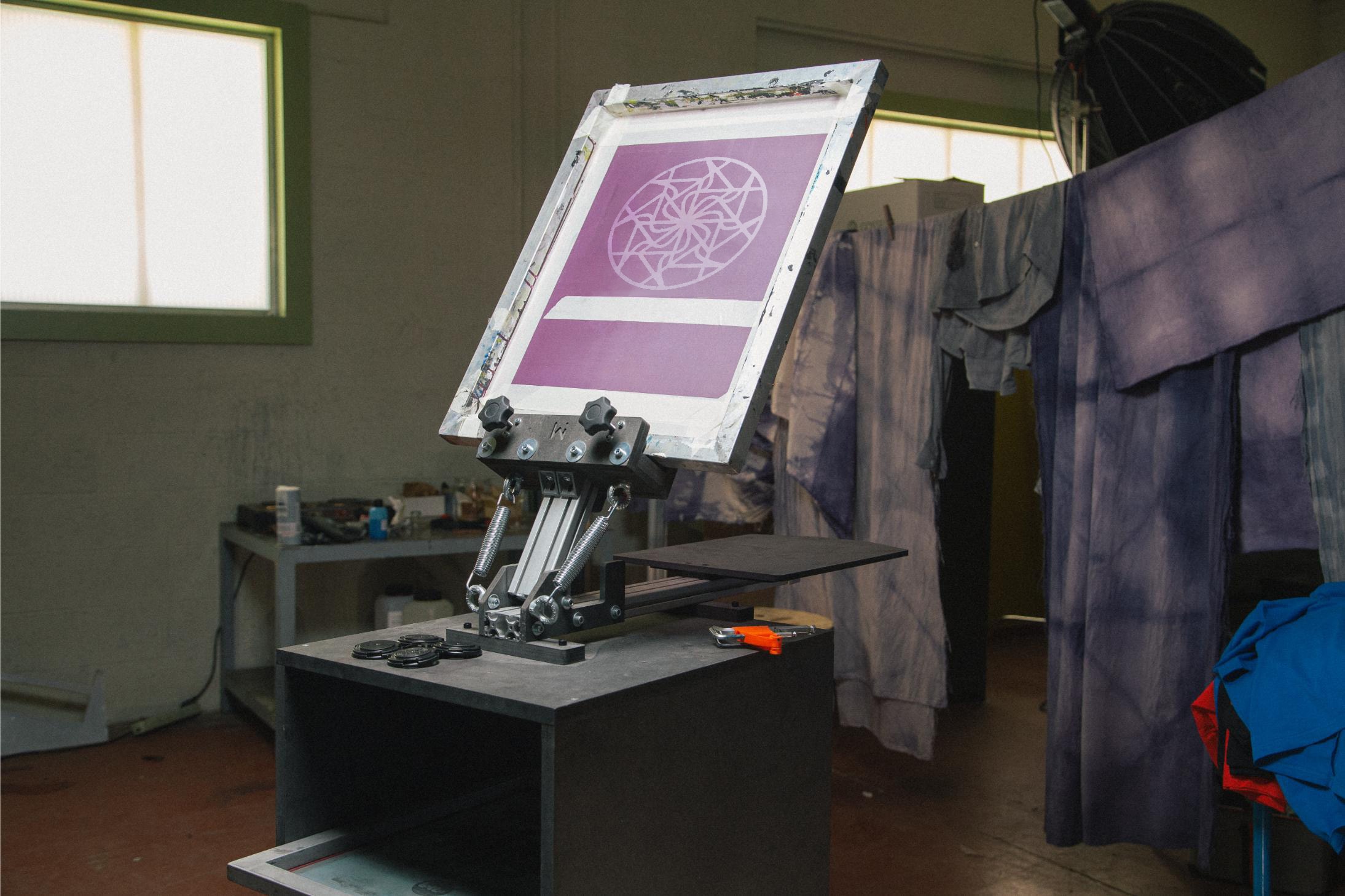 Screen Printing press with design on the screen ready to print in a screenprinting workshop with fabric in the background