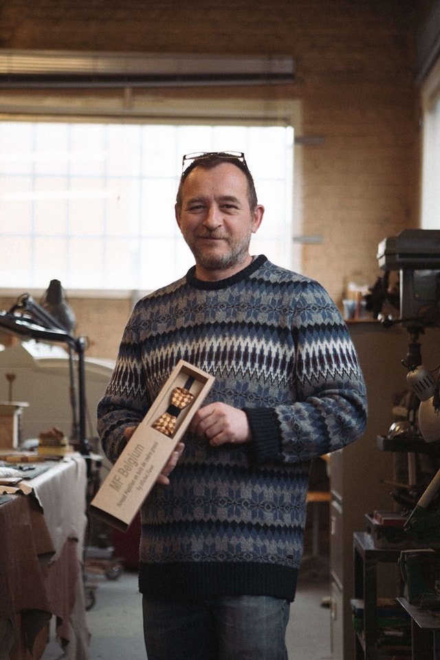 Michel Faye standing with his wooden bow ties in his workshop