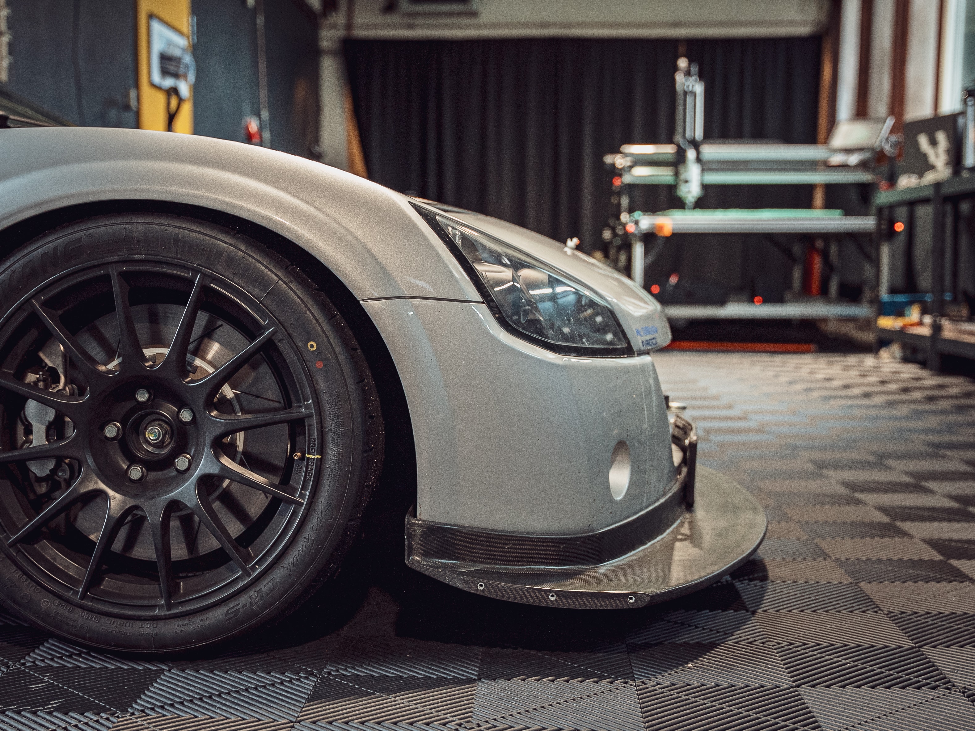 Fancy silver sport car front with a CNC milling machine in the background