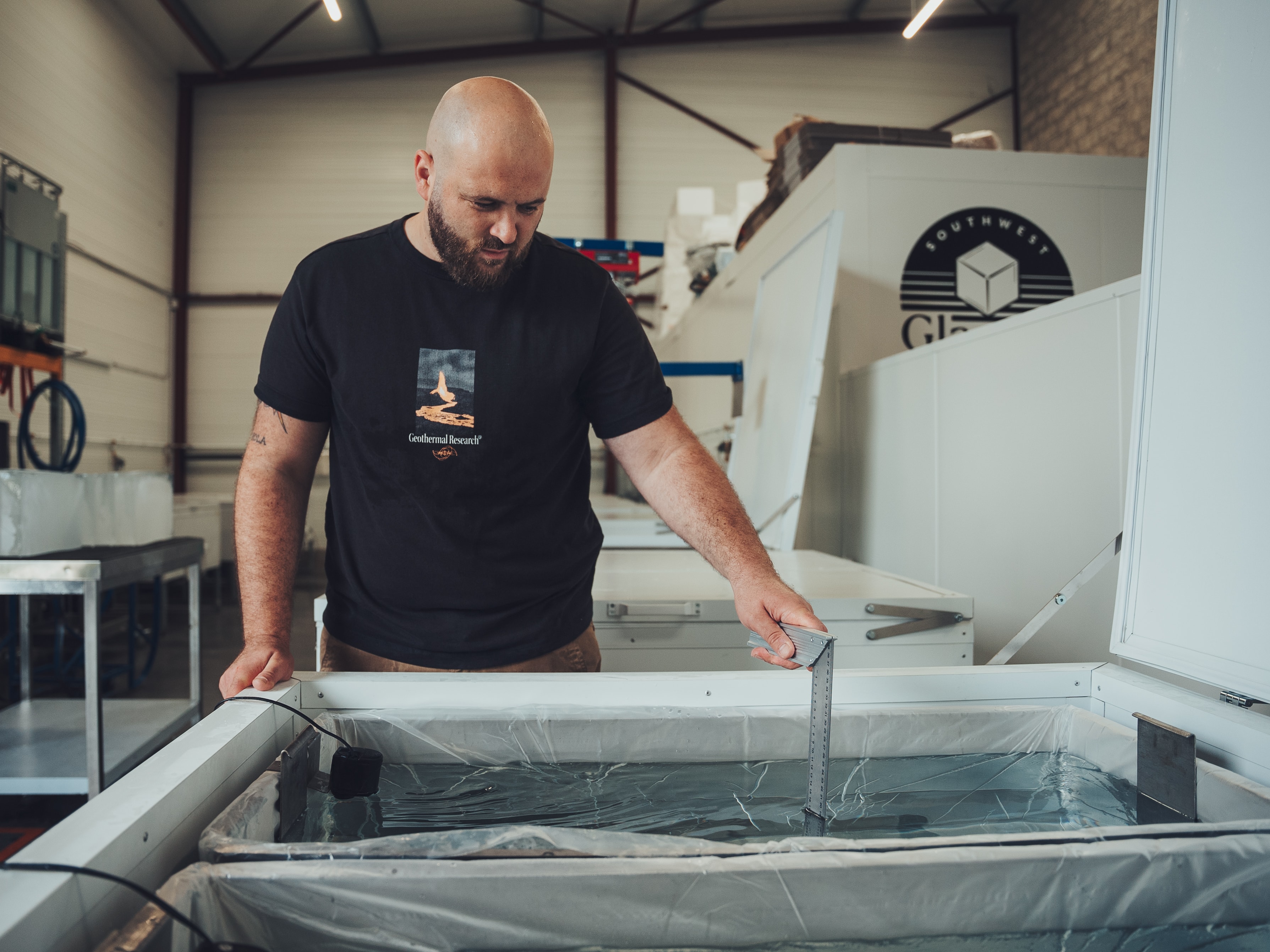 Employee measuring the depth of ice in a profesional ice creating machine placed in a cold chamber