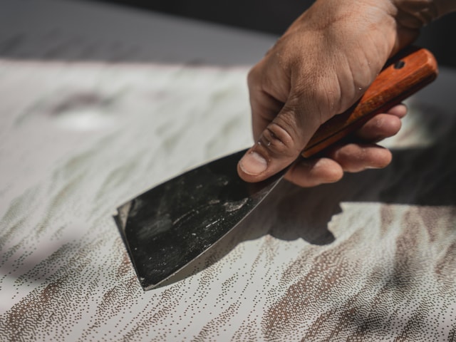 close-up on a hand scrapping the surface of a milled OSB panel with a painter knife
