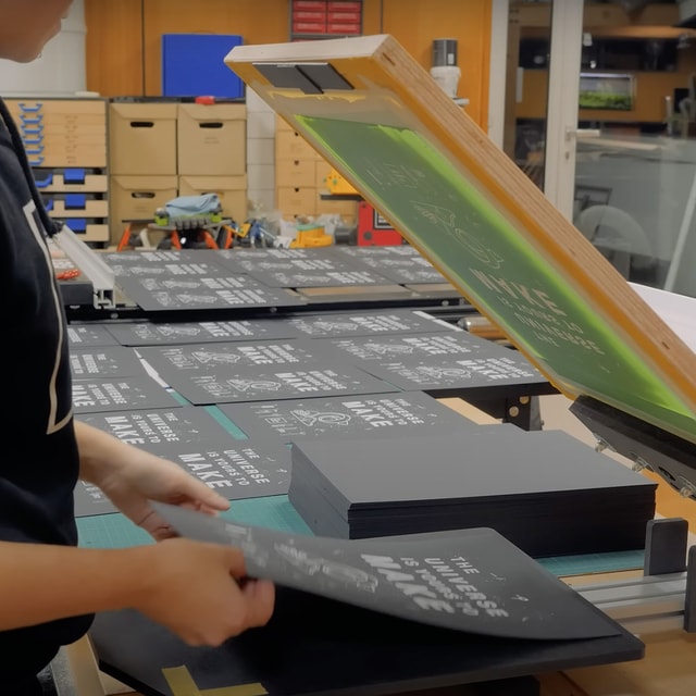 Hands printing black posters with Mekanika screen printing press